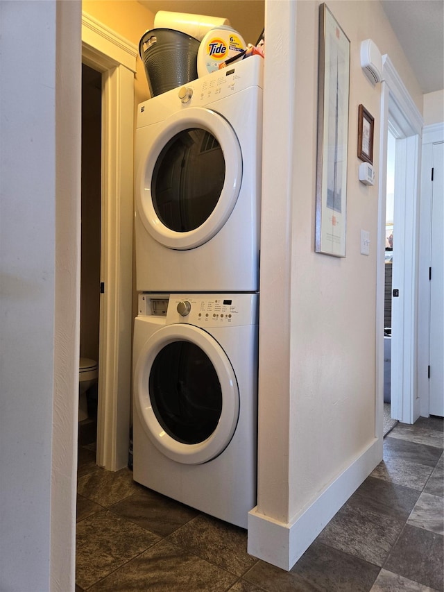 washroom with stacked washer and dryer, laundry area, stone finish flooring, and baseboards