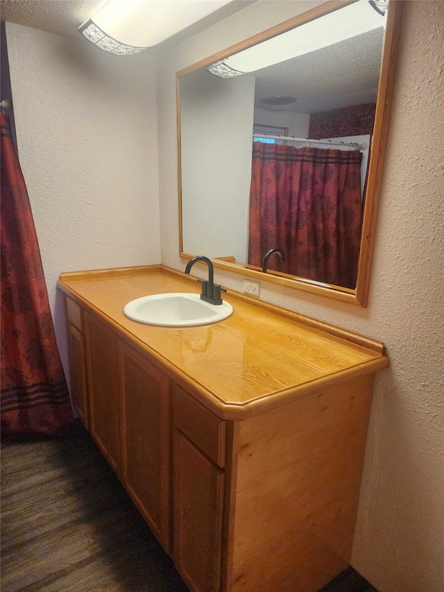 full bathroom featuring a textured wall, wood finished floors, and vanity