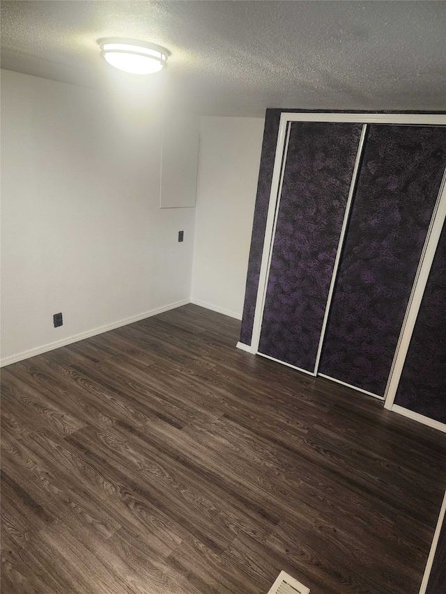 unfurnished bedroom featuring a closet, a textured ceiling, baseboards, and dark wood-style flooring