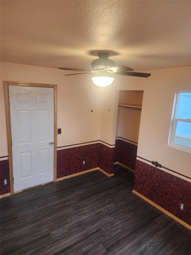 unfurnished room featuring dark wood-style flooring, a wainscoted wall, ceiling fan, and a textured ceiling