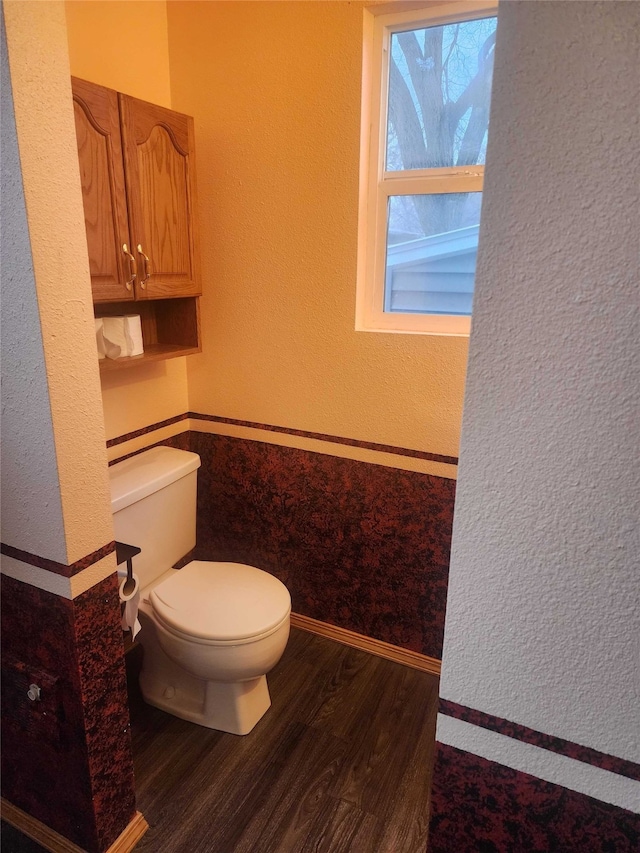 bathroom featuring toilet, baseboards, wood finished floors, and a textured wall