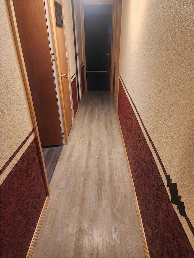 hallway featuring light wood-type flooring, visible vents, and a textured wall