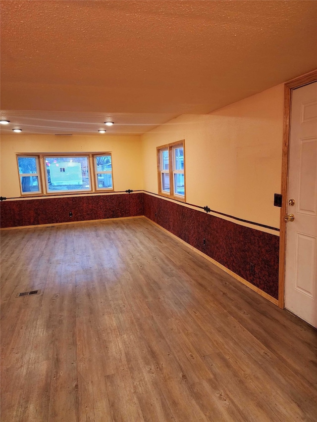 unfurnished room featuring a wainscoted wall, a textured ceiling, wood finished floors, and visible vents