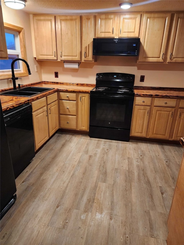 kitchen with light brown cabinets, a sink, light wood finished floors, and black appliances