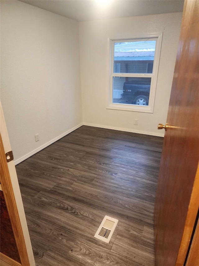 empty room featuring visible vents, dark wood finished floors, and baseboards