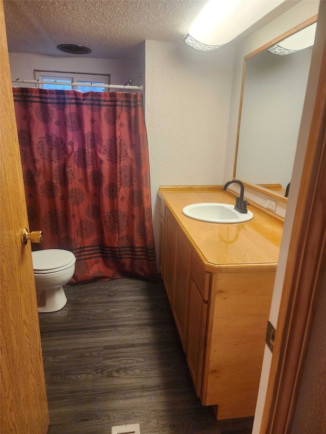 full bath featuring a shower with shower curtain, toilet, wood finished floors, a textured ceiling, and vanity