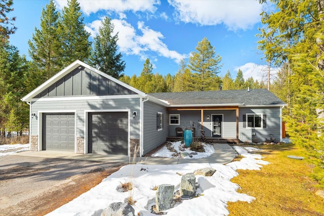 view of front of home featuring driveway, stone siding, an attached garage, covered porch, and board and batten siding