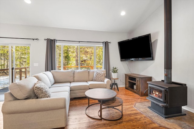 living room with baseboards, wood finished floors, a wood stove, vaulted ceiling, and recessed lighting