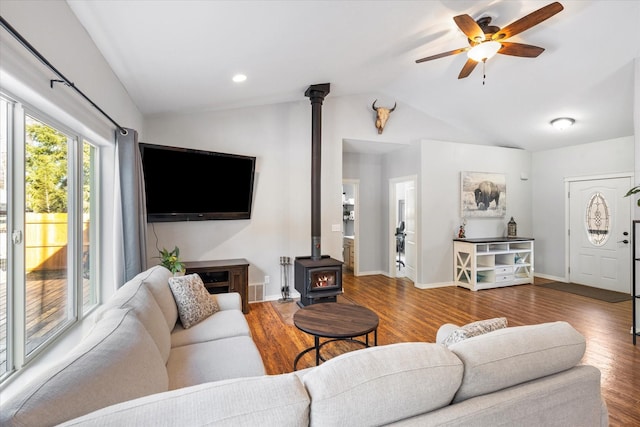 living area featuring lofted ceiling, ceiling fan, wood finished floors, baseboards, and a wood stove