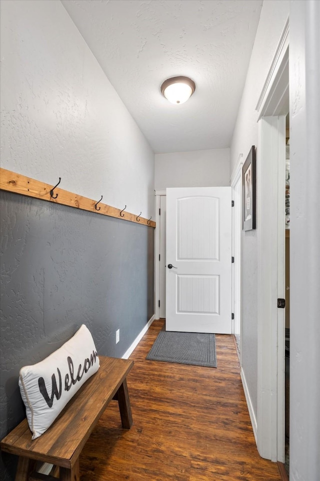 doorway with baseboards, wood finished floors, and a textured wall