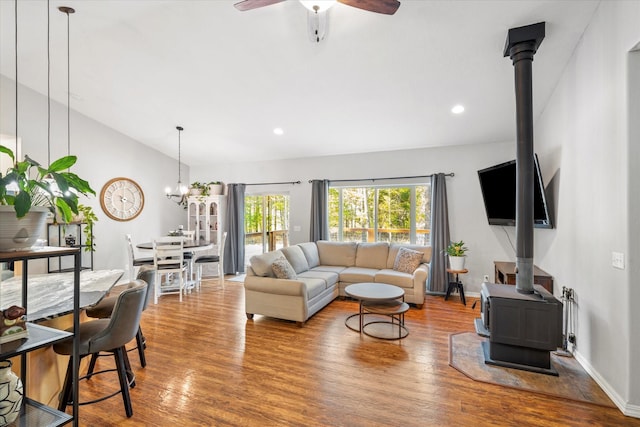 living area with a wealth of natural light, a wood stove, vaulted ceiling, and wood finished floors