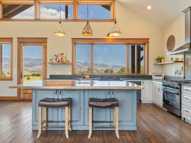 kitchen featuring high end stove, white cabinetry, hanging light fixtures, wall chimney range hood, and open shelves