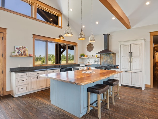 kitchen with open shelves, wall chimney range hood, butcher block countertops, beamed ceiling, and a kitchen bar