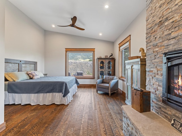 bedroom with dark wood-style floors, vaulted ceiling, a stone fireplace, ceiling fan, and baseboards