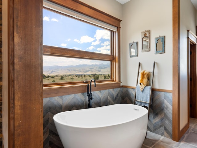 bathroom with a mountain view, wainscoting, a soaking tub, and tile walls