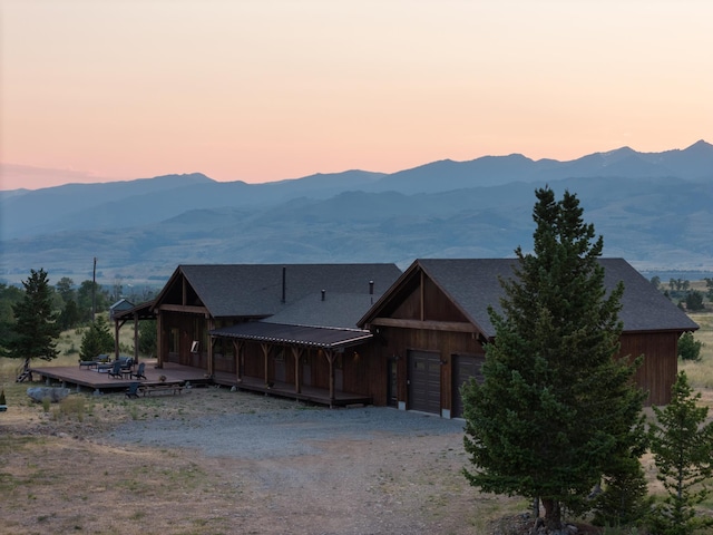 view of front of home with a garage, driveway, a deck with mountain view, and a shingled roof