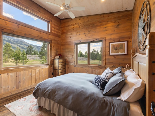 bedroom with a ceiling fan, wood walls, and wood finished floors