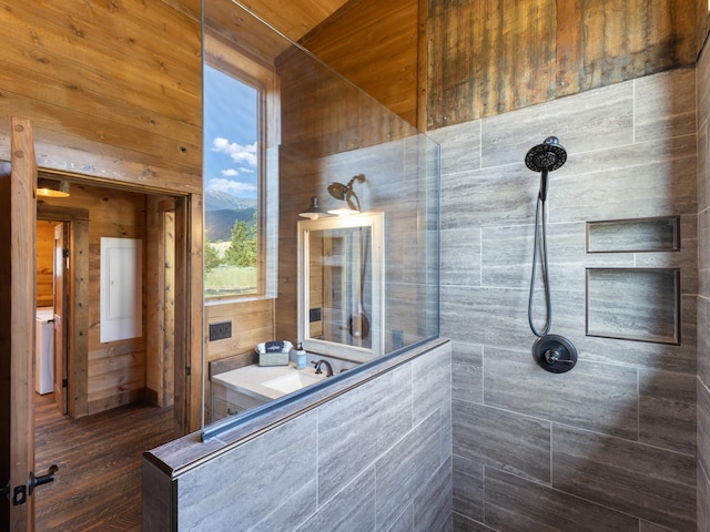 full bathroom with wood walls, a tile shower, and vanity