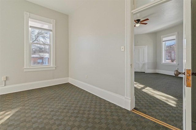 spare room with a ceiling fan, dark colored carpet, plenty of natural light, and baseboards