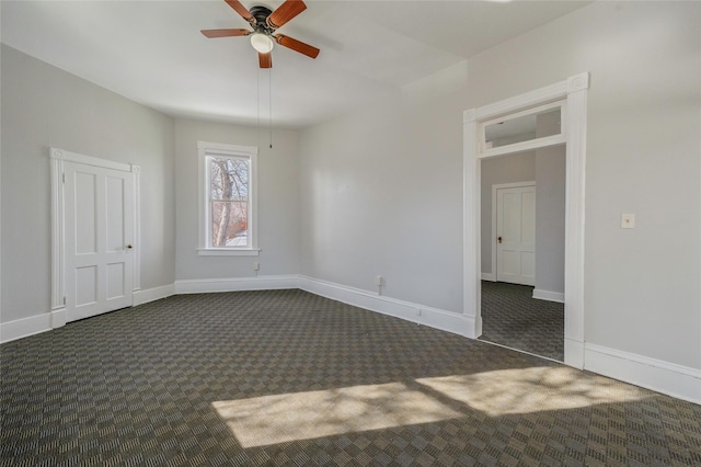 unfurnished room with dark colored carpet, a ceiling fan, and baseboards