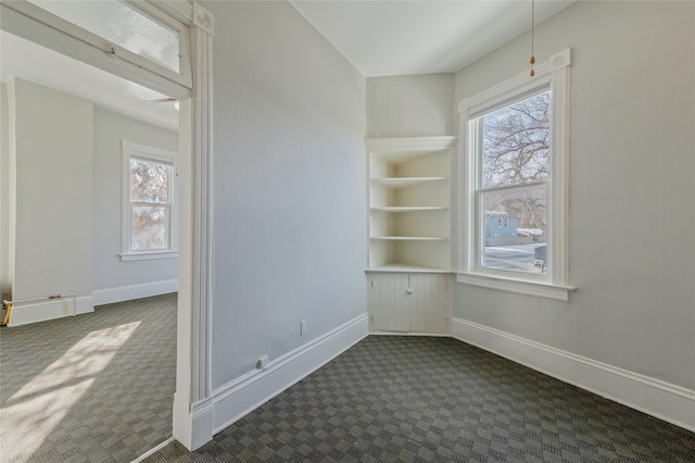 spare room with built in shelves, baseboards, and dark colored carpet