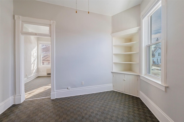 spare room featuring dark colored carpet and baseboards