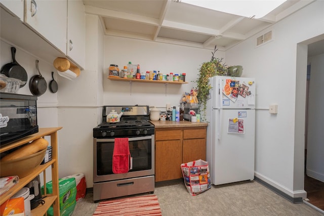 kitchen with light countertops, visible vents, brown cabinetry, freestanding refrigerator, and stainless steel range with gas stovetop