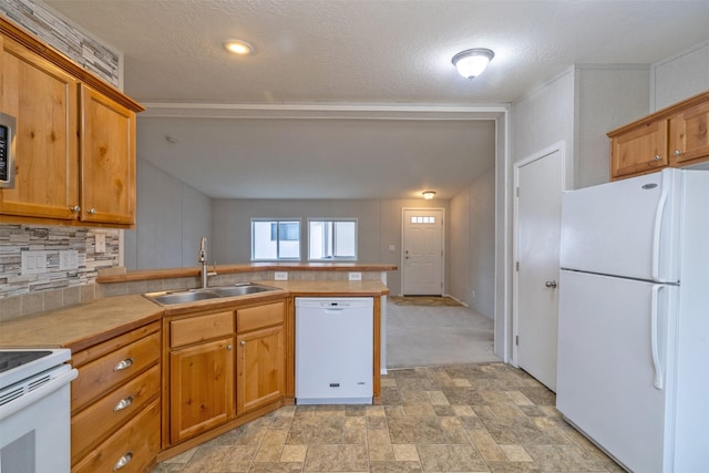 kitchen featuring white appliances, brown cabinetry, a peninsula, a sink, and backsplash