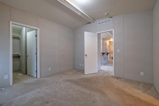 carpeted empty room featuring visible vents, lofted ceiling with beams, and a textured ceiling