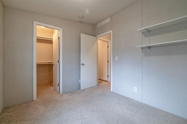 unfurnished bedroom with carpet, visible vents, a walk in closet, and a closet