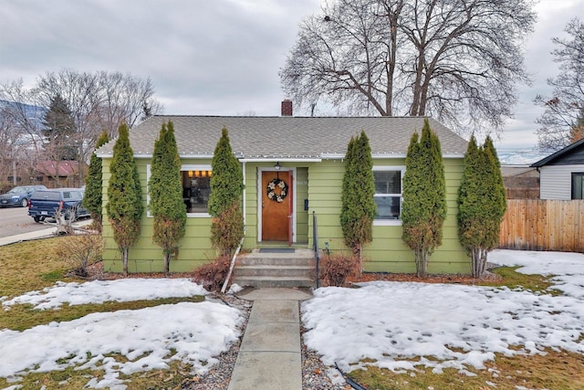 bungalow-style house featuring a shingled roof, a chimney, and fence