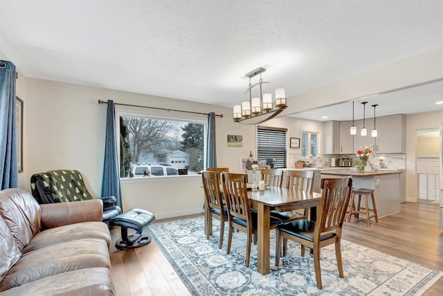 dining room with light wood finished floors, a textured ceiling, baseboards, and a notable chandelier