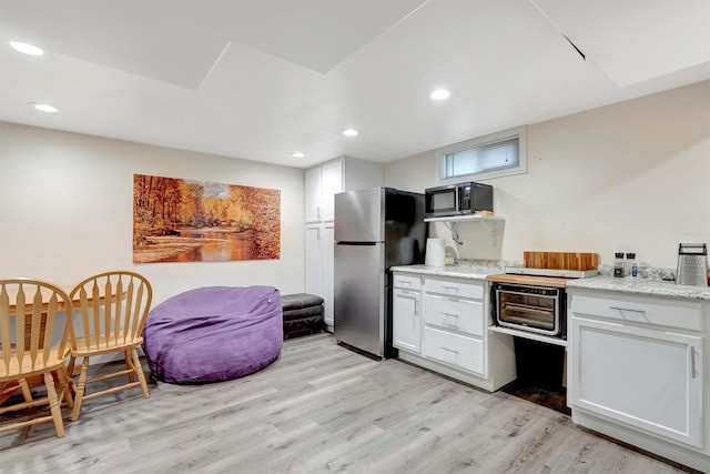 kitchen with white cabinets, freestanding refrigerator, light wood-style floors, black microwave, and recessed lighting