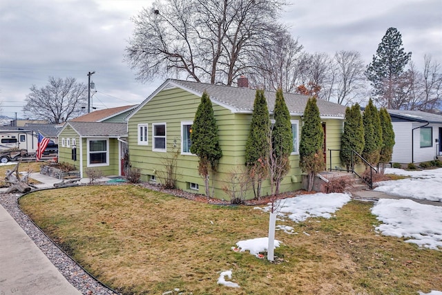 view of front facade with a shingled roof, a chimney, and a front lawn