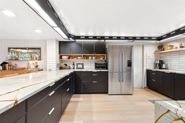 kitchen featuring open shelves, stainless steel fridge, tasteful backsplash, and dark cabinetry