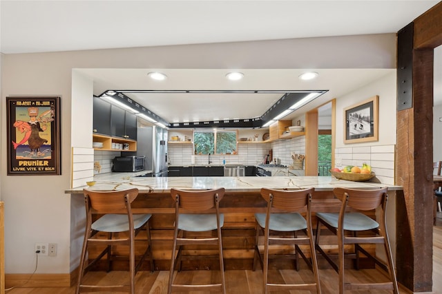 kitchen with open shelves, a peninsula, backsplash, and a sink