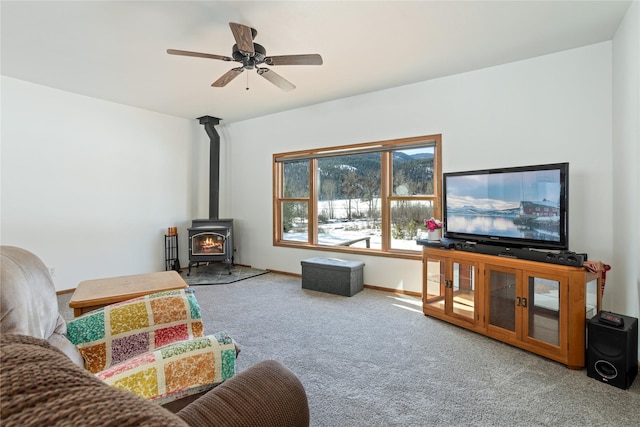 carpeted living room with a wood stove, ceiling fan, and baseboards