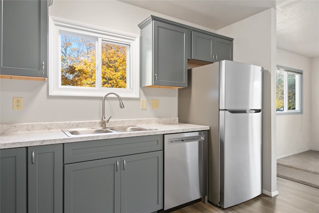 kitchen with gray cabinetry, appliances with stainless steel finishes, a sink, wood finished floors, and baseboards