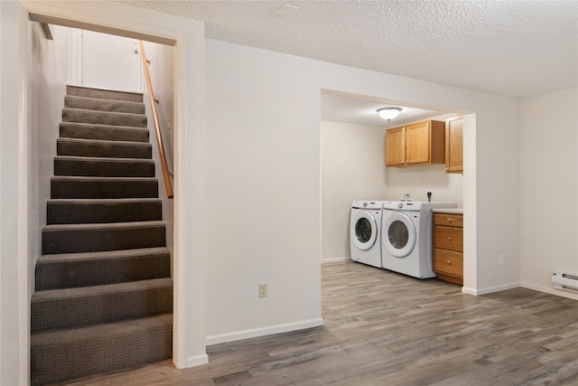 washroom with cabinet space, baseboards, wood finished floors, a textured ceiling, and washing machine and dryer