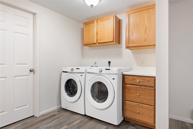 washroom featuring cabinet space, baseboards, wood finished floors, washing machine and clothes dryer, and a textured ceiling