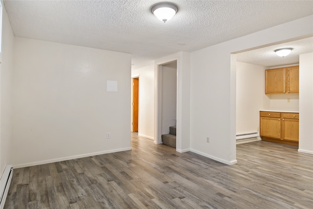 spare room featuring a baseboard radiator, stairway, baseboards, and wood finished floors