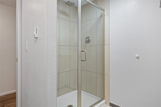 full bathroom featuring a textured wall, a shower stall, baseboards, and wood finished floors