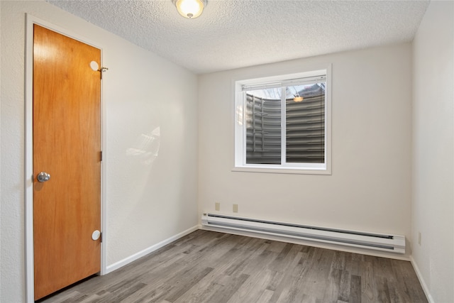 unfurnished room with a textured ceiling, baseboards, baseboard heating, and wood finished floors