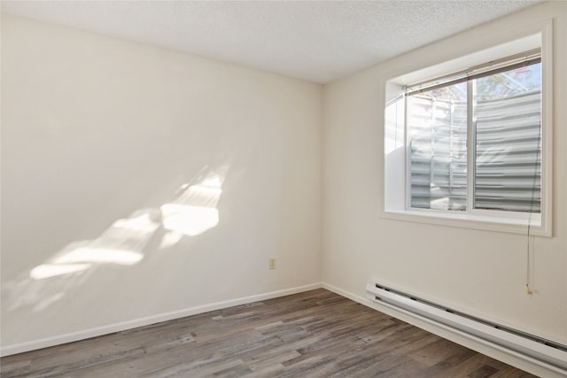 empty room with a textured ceiling, baseboard heating, wood finished floors, and baseboards