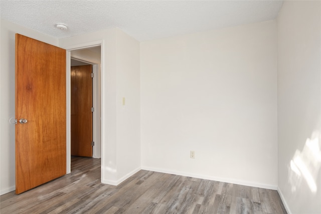 spare room with a textured ceiling, wood finished floors, and baseboards