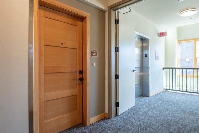 hall with elevator, baseboards, and dark colored carpet