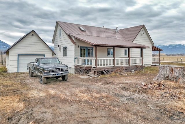 back of house featuring metal roof, a mountain view, covered porch, a detached garage, and dirt driveway