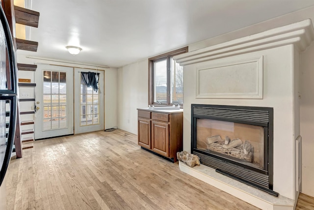 unfurnished living room featuring light wood-style flooring, french doors, and a glass covered fireplace