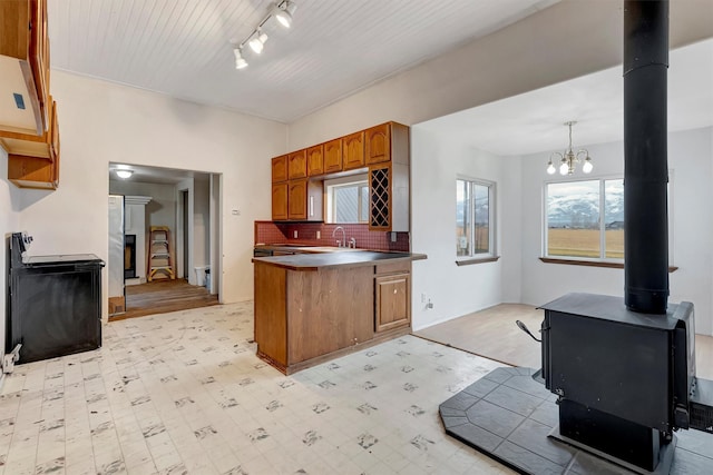 kitchen featuring a peninsula, decorative backsplash, light floors, brown cabinetry, and a wood stove