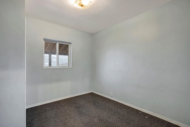 unfurnished room featuring dark carpet and baseboards